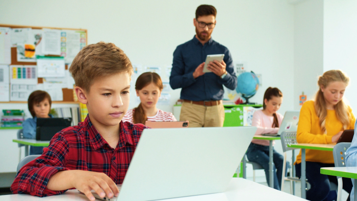 An male students focuses on his computer while a teacher looks over his shoulder.