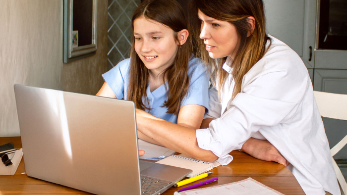A tween girl and woman caregiver look at a laptop screen together.