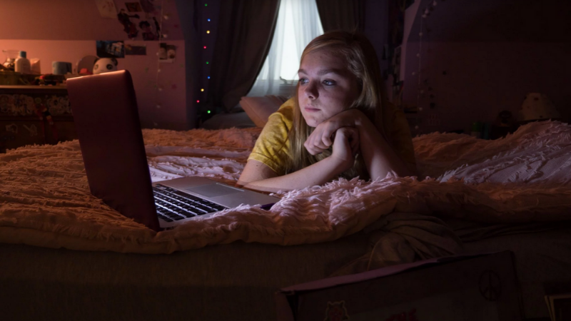 Still from the movie showing girl on her bed looking at a laptop