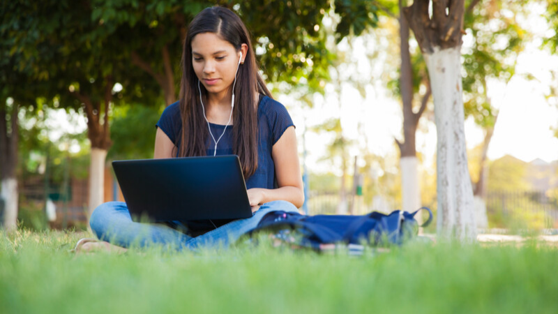 teen girl reading on her laptop outside