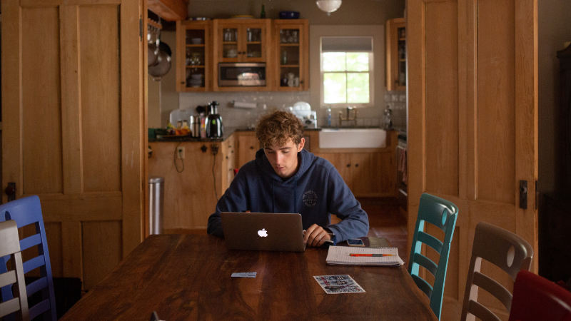 Teenage boy sitting at a kitchen table with a laptop
