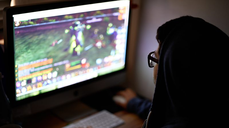 Teen in a hoodie playing an online game on a computer.