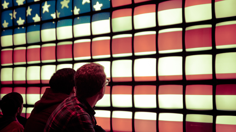 Photo of a person gazing at a wall of televisions with the American flag
